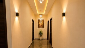 Un pasillo con candelabro, luces en la pared, una planta en maceta y puertas.