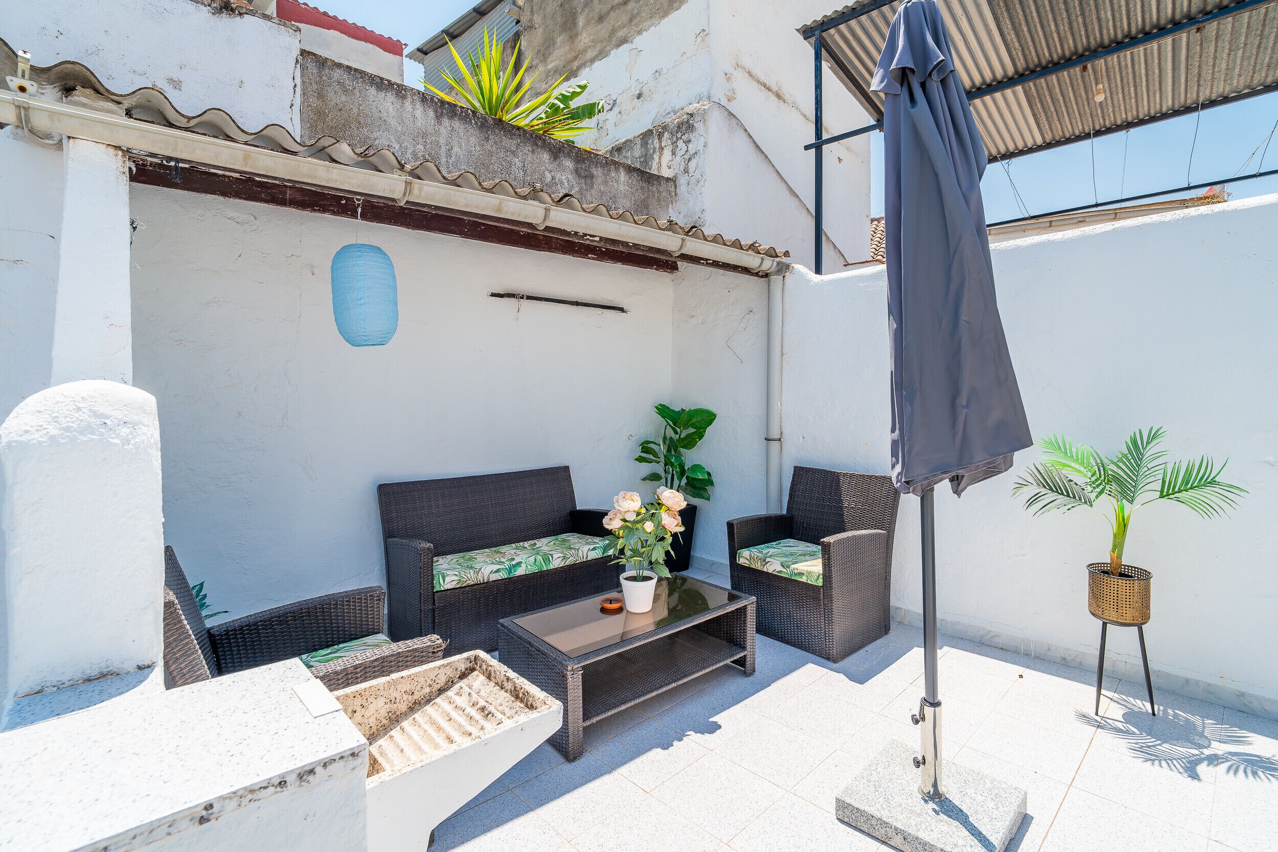 Un patio con mobiliario de mimbre, una mesa y plantas en macetas.