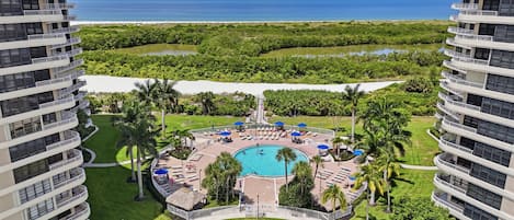 Um hotel moderno com piscina central, cercado por espreguiçadeiras e guarda-sóis, com vista para uma praia e oceano.
