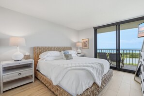 Ein Schlafzimmer mit einem Bett, Nachttischen, einer Lampe, einem Gemälde und einem Balkon mit Blick.