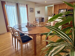 A dining area with a wooden table and chairs, a kitchen in the background, and a large potted plant. - Walk to The Barlow & Downtown  -  Bright 2BR/2BA Wine Country Retreat (Sebastopol)