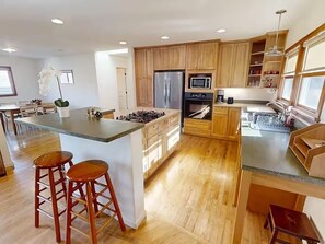 A modern kitchen with wooden cabinets, a central island with stools, and a built-in stove. - Walk to The Barlow & Downtown  -  Bright 2BR/2BA Wine Country Retreat (Sebastopol)