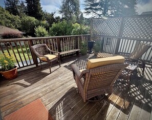 A wooden deck with wicker furniture, including a chair and a table, surrounded by potted plants and a lattice fence. - Walk to The Barlow & Downtown  -  Bright 2BR/2BA Wine Country Retreat (Sebastopol)