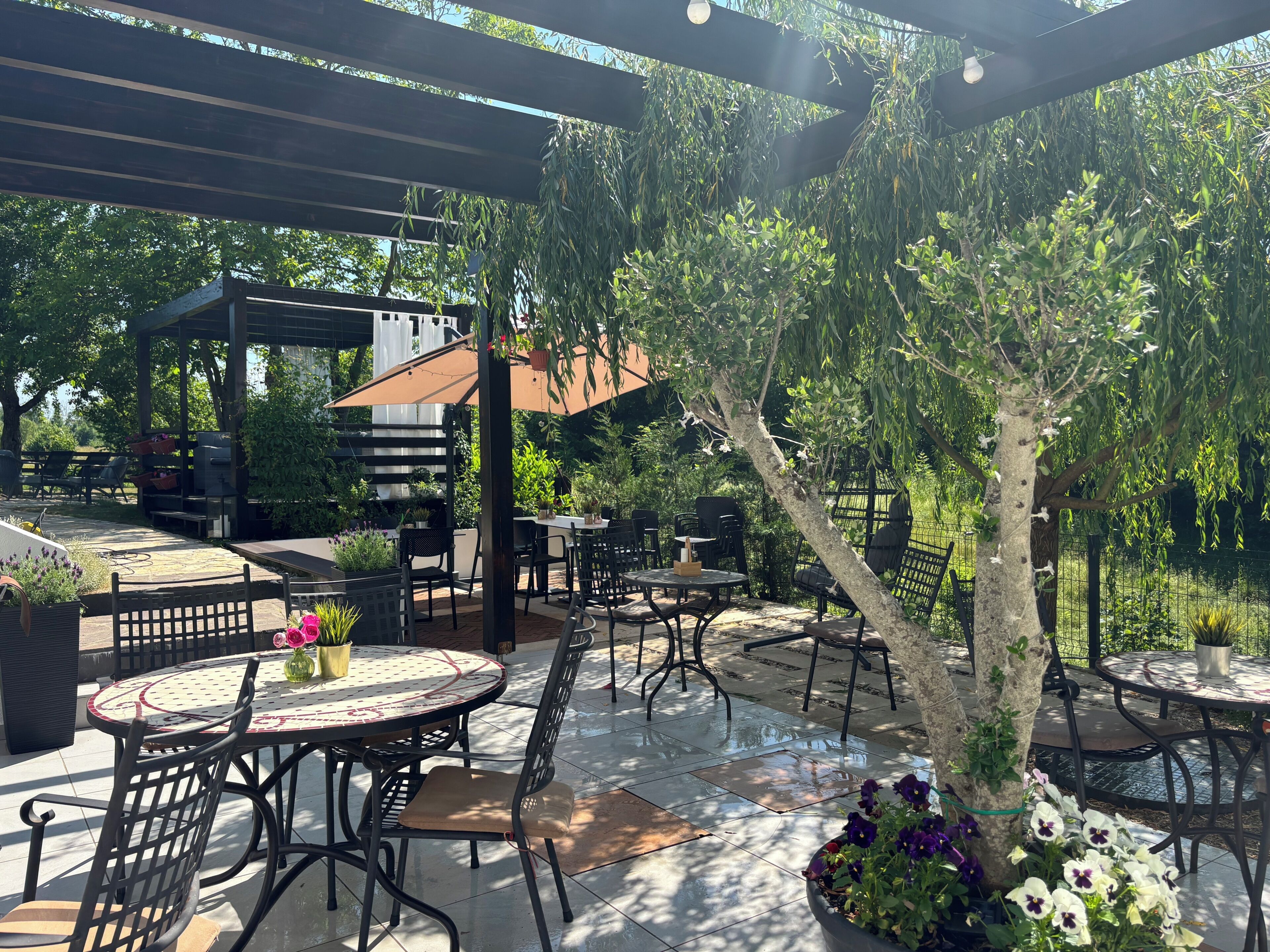 An outdoor patio with round tables and chairs, a pergola, and a grill area.