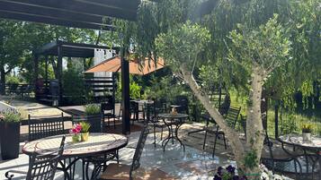 An outdoor patio with round tables and chairs, a pergola, and a grill area.