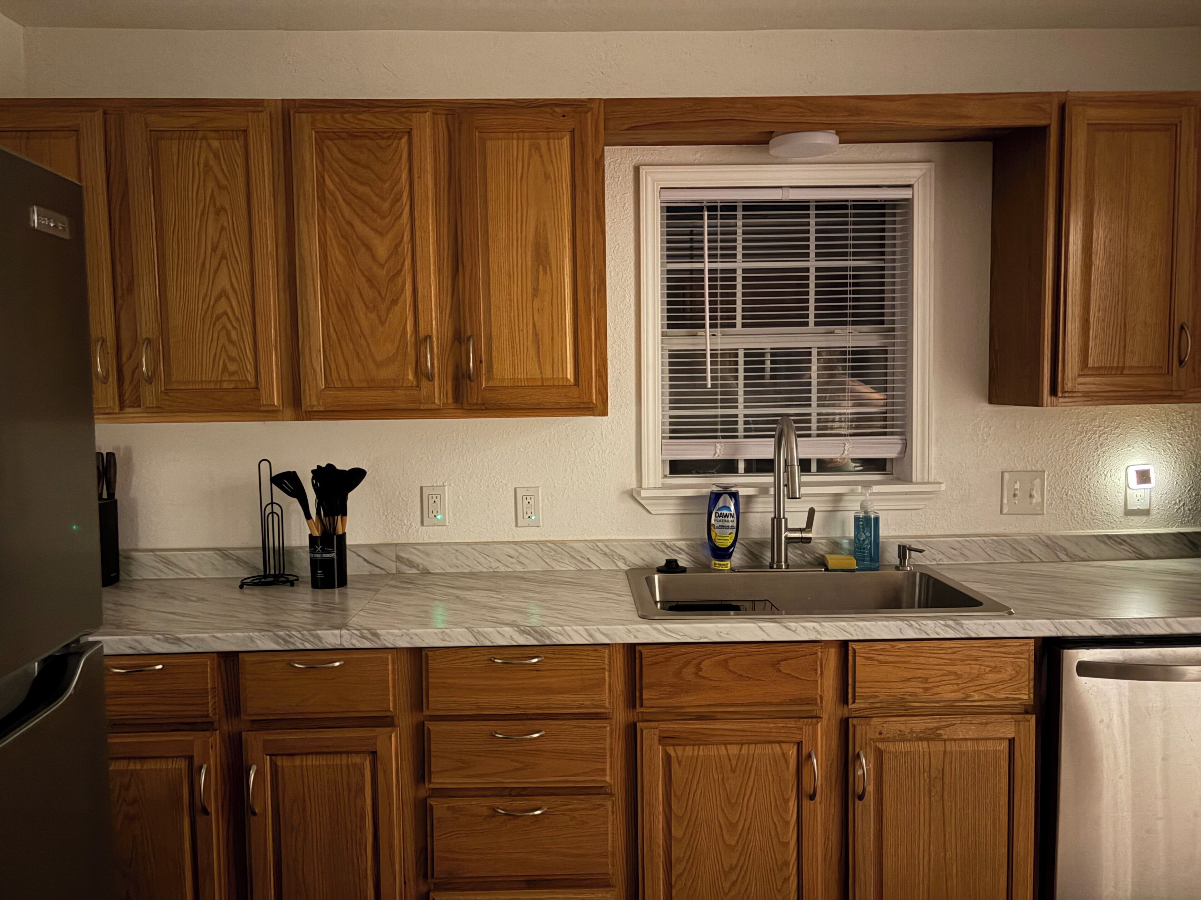 A kitchen with wooden cabinets, a stainless steel sink, and a window with blinds.
