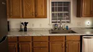 A kitchen with wooden cabinets, a stainless steel sink, and a window with blinds. - Route 66 Retreat (Vega)