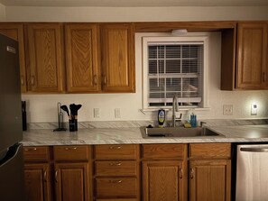 A kitchen with wooden cabinets, a stainless steel sink, and a window with blinds. - Route 66 Retreat (Vega)