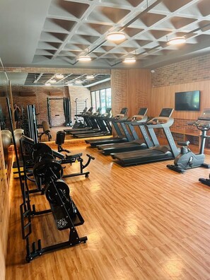 Uma academia com esteiras, aparelhos de musculação e piso de madeira.