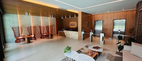 A modern hotel lobby with a reception desk, seating area, and elevators.