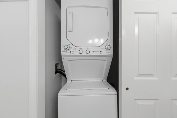 Une machine à laver à chargement frontal, située dans une buanderie avec une porte blanche et un mur blanc.