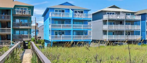 A beachfront property with multiple-story buildings, a boardwalk, and a sandy path leading to the beach.