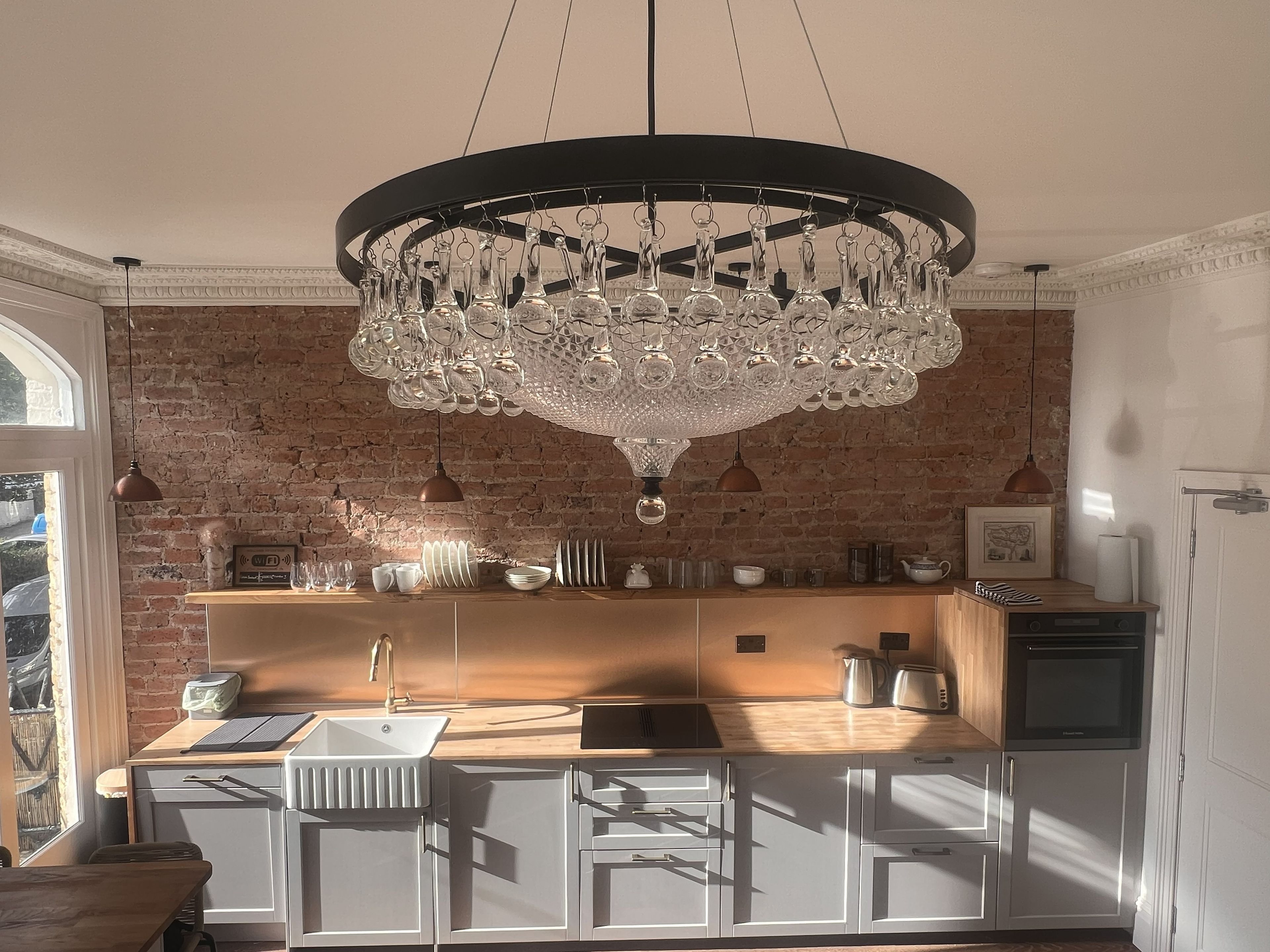A modern kitchen with a brick wall, a chandelier, and a wooden island with a sink.