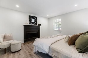 Ein Schlafzimmer mit Bett, Stuhl, Kamin und Fenster.