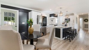 A modern kitchen with a central island, bar stools, and a dining area with chairs. - Home Away From Home in Nashville 3B 2B W/ Large Fenced in Back Yard (Nashville)