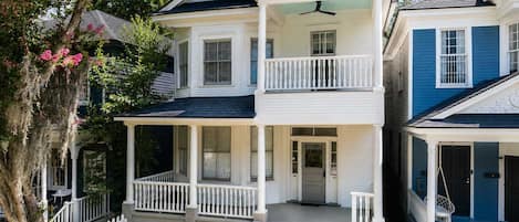 A two-story house with a front porch, a balcony, and a white picket fence.