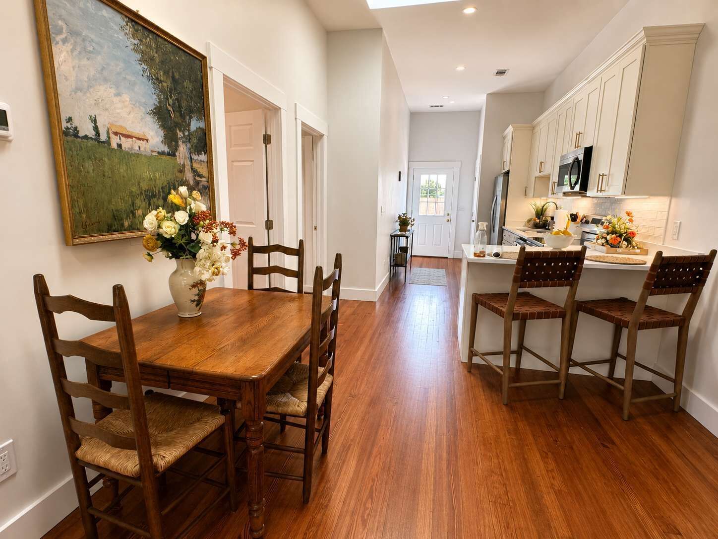 A dining area with a wooden table and chairs, a vase of flowers, and a painting on the wall.
