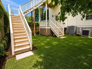 A residential property with a wooden staircase leading to a deck, a well-maintained lawn, and an air conditioning unit. - Stunning Home Near Starland | 2 King Beds (Savannah)