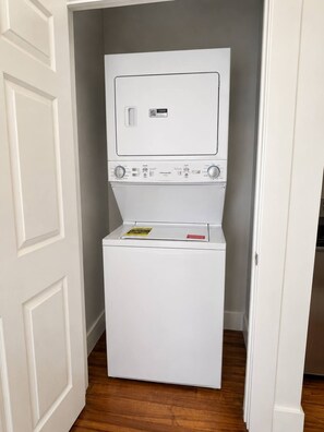 A compact, white, front-loading washer and dryer unit in a narrow hallway with wooden flooring. - Stunning Home Near Starland | 2 King Beds (Savannah)