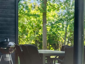 Eine Holzterrasse mit Tisch, Stühlen, Grill und Blick auf eine bewaldete Landschaft.