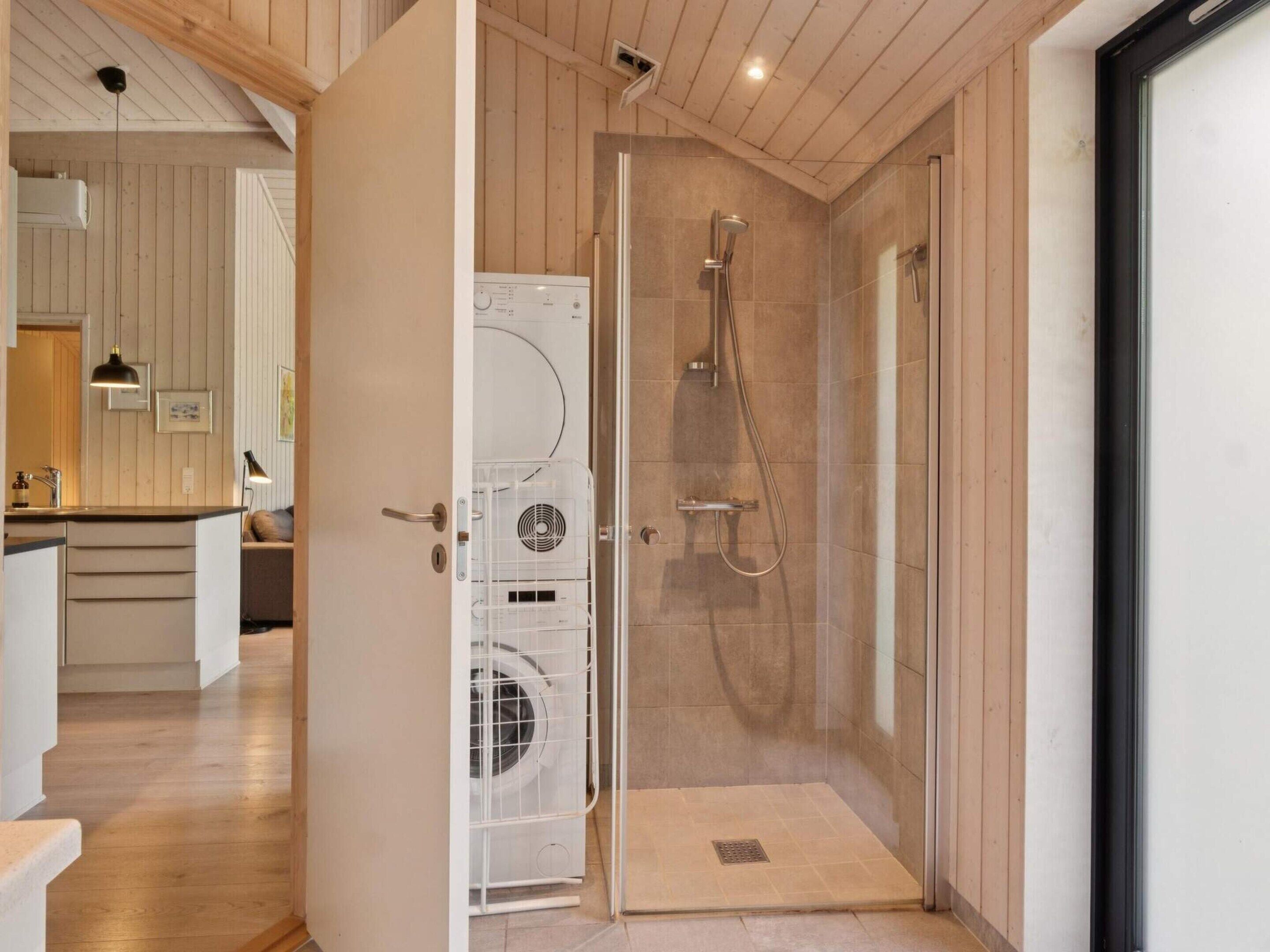 A modern bathroom with a glass-enclosed shower, a built-in washing machine, and a wooden interior.