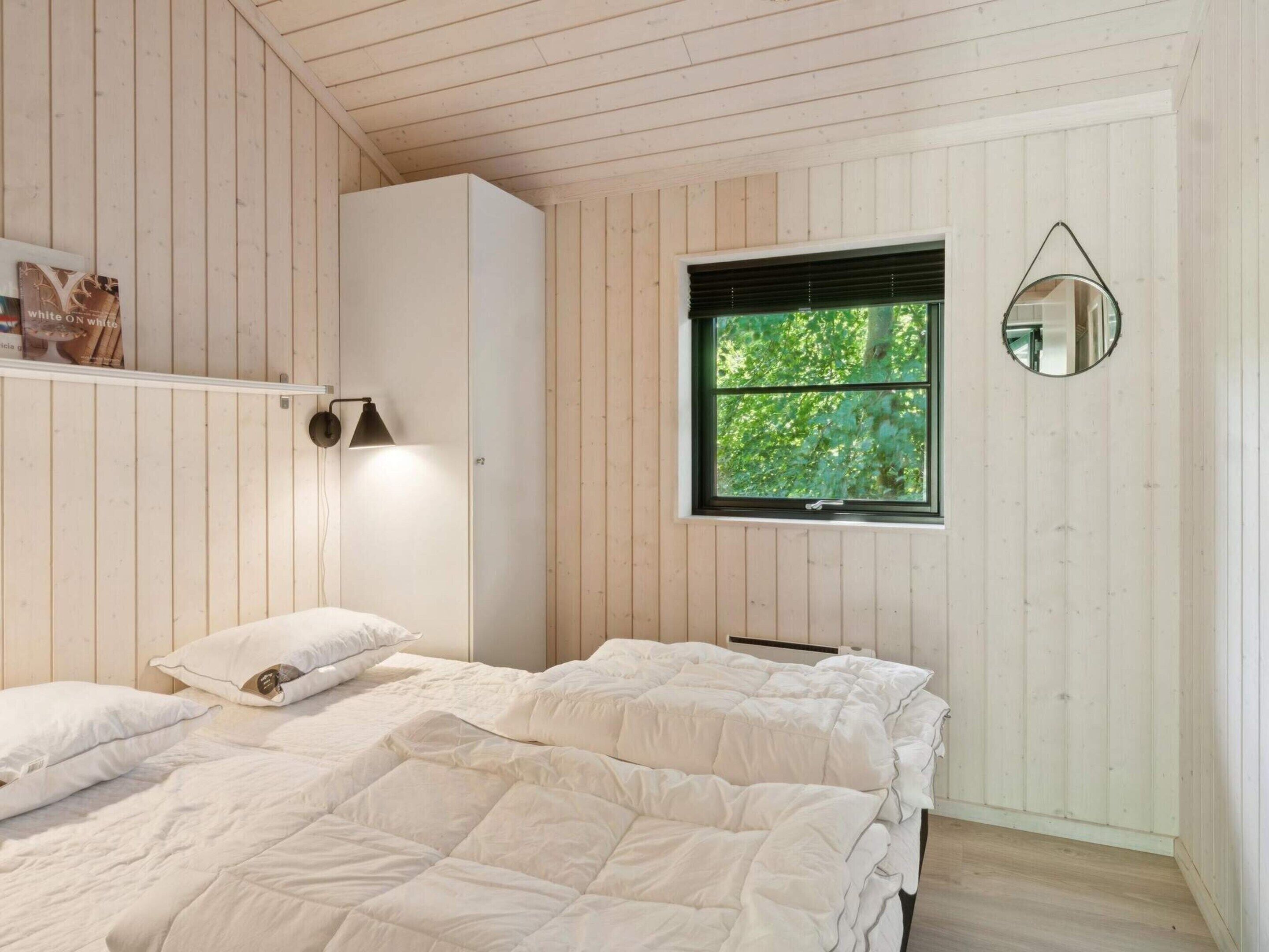 Een slaapkamer met twee bedden, een kledingkast, een raam met uitzicht op groen en een spiegel aan de muur.