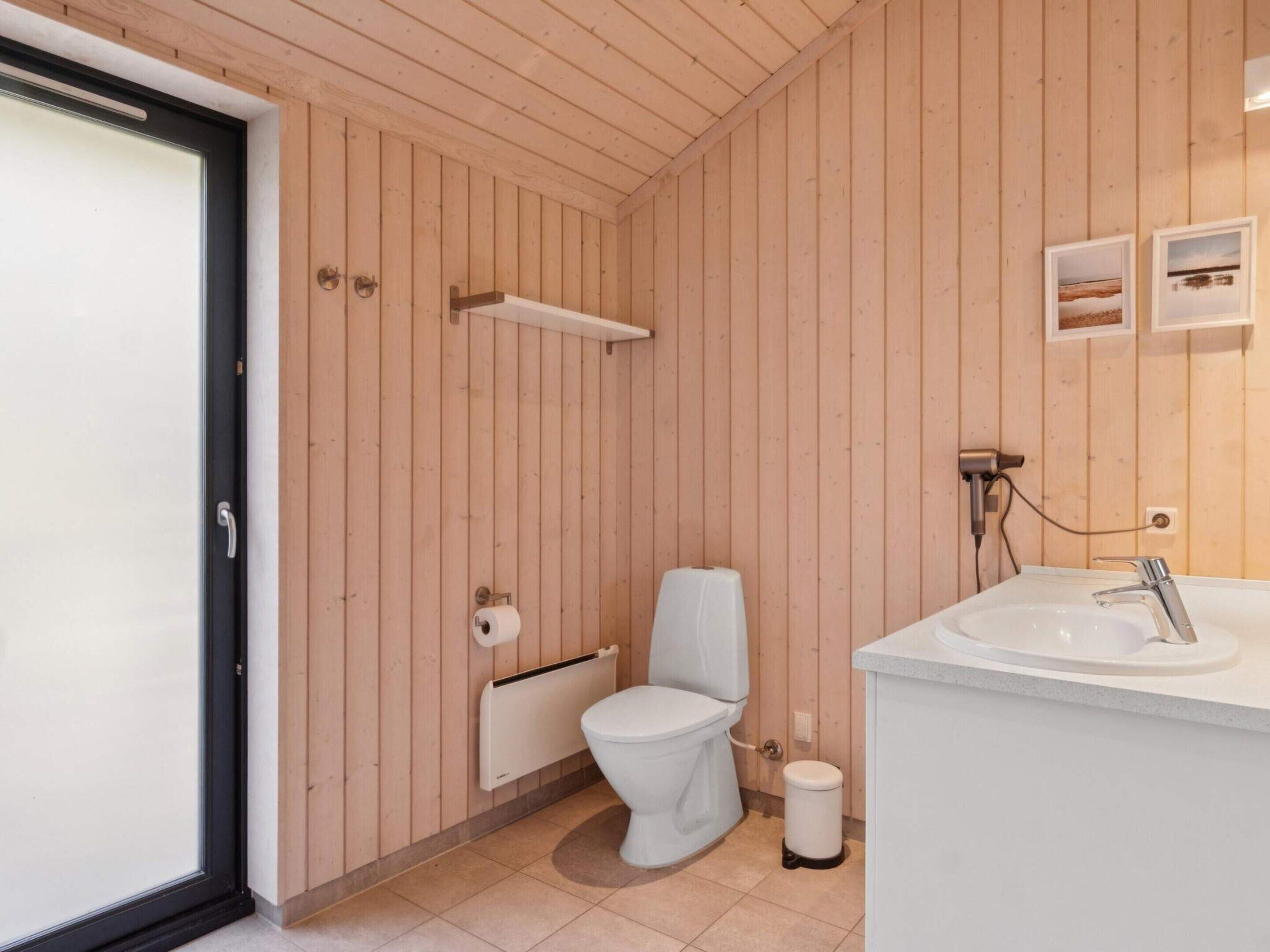 A modern bathroom with wooden paneling, a toilet, a sink, and a towel rack.
