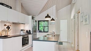 A modern kitchen with white cabinetry, a central island, pendant lighting, and a view through the window. - 4 Star Holiday Home in Vig (Vig)