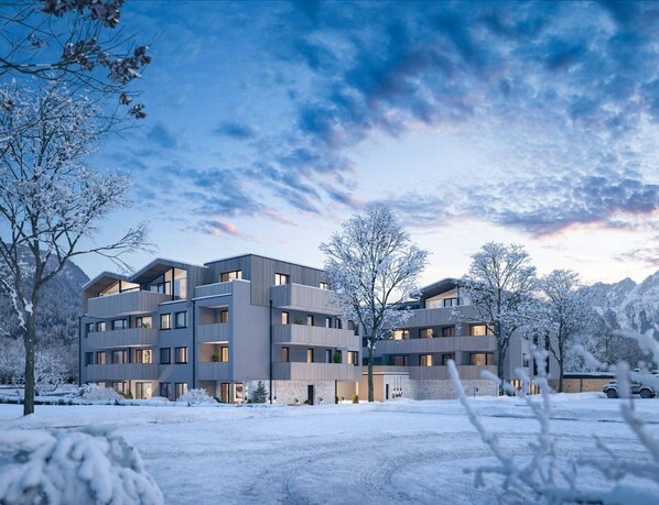 Ein modernes, mehrstöckiges Gebäude mit Balkonen, umgeben von schneebedeckten Bäumen und Bergen im Hintergrund.