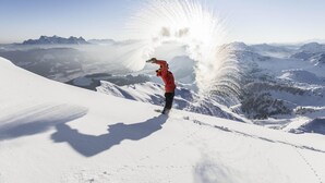 Een persoon staat op een besneeuwde bergtop, de lucht is helder.