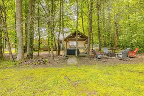 Eine Holzhütte mit Veranda, umgeben von Bäumen, mit Sitzgelegenheiten inklusive Stühlen und einem Feuerkorb.