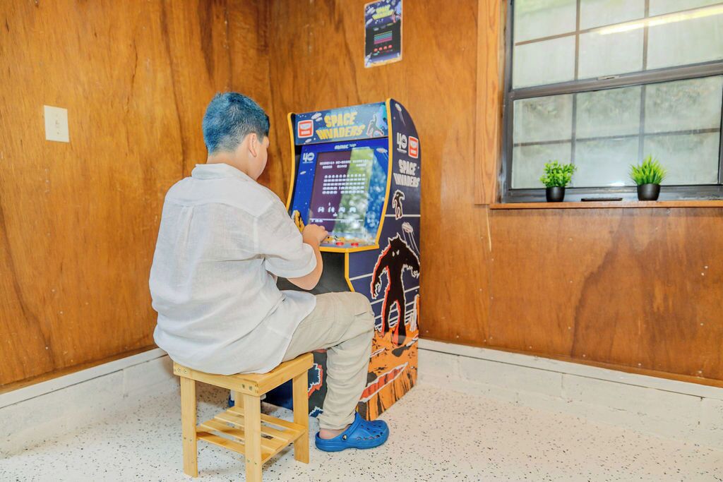 A person sitting on a wooden stool in front of a space-themed arcade game machine.