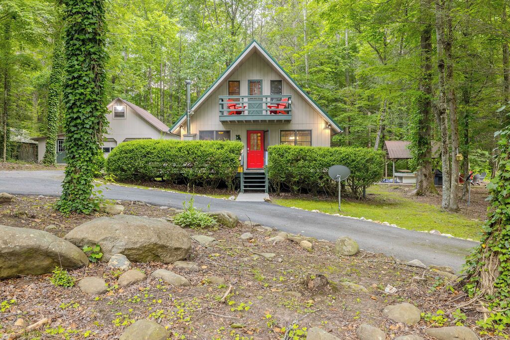 A cabin with a red door, a balcony with red chairs, surrounded by trees and a road.