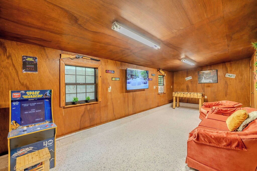 A room with wooden walls, a television, a Space Invaders game, a window, and a sofa.