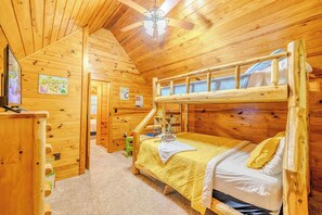 Ein Zimmer in einer Holzhütte mit Etagenbetten, einem Deckenventilator und einem Fernseher.
