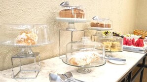 Une table de buffet proposant divers plats, notamment des gâteaux et des pâtisseries, ainsi que les ustensiles de service.