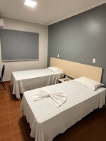 Habitación de hotel con dos camas individuales, una mesita pequeña, una silla y un ventanal grande.