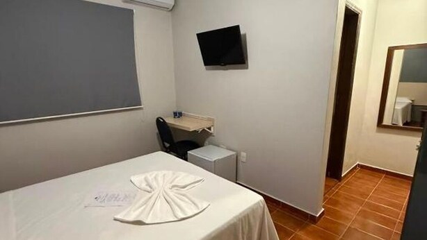 Une petite pièce comprenant un lit, un bureau, une chaise, un téléviseur à écran plat et un miroir.