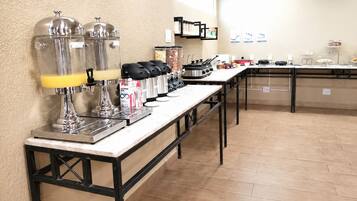 Montaje de bufé con estaciones de autoservicio, incluyendo máquinas de café y una variedad de alimentos.