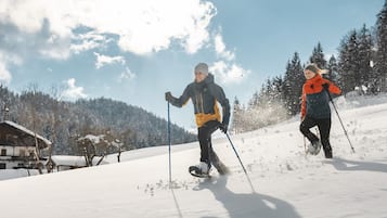 Zwei Personen sind auf einem verschneiten Hang beim Skifahren, am Himmel ist es klar und im Hintergrund sind Bäume zu sehen.