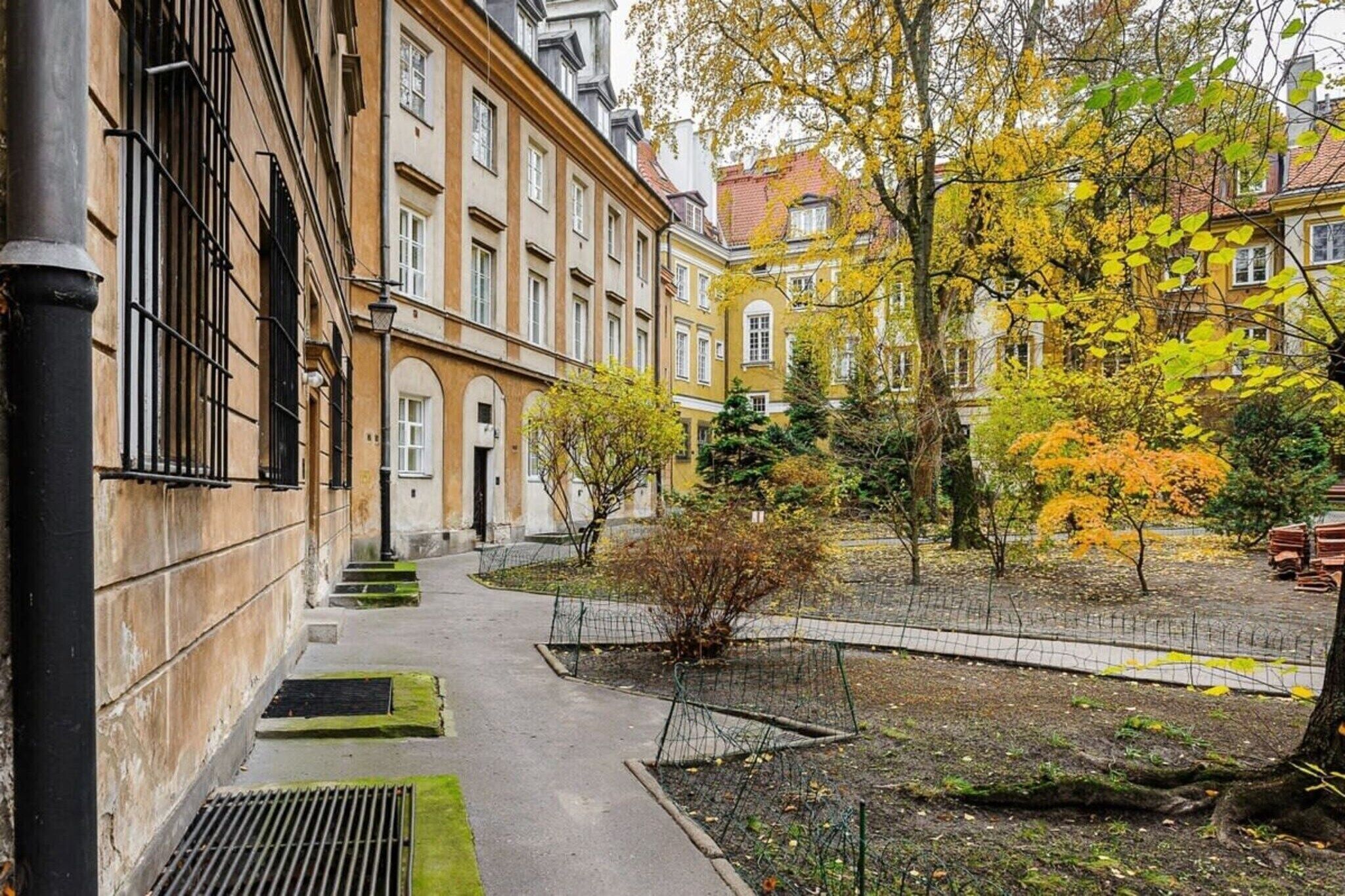 A courtyard with a pathway leading to a building entrance, surrounded by trees with autumn foliage.