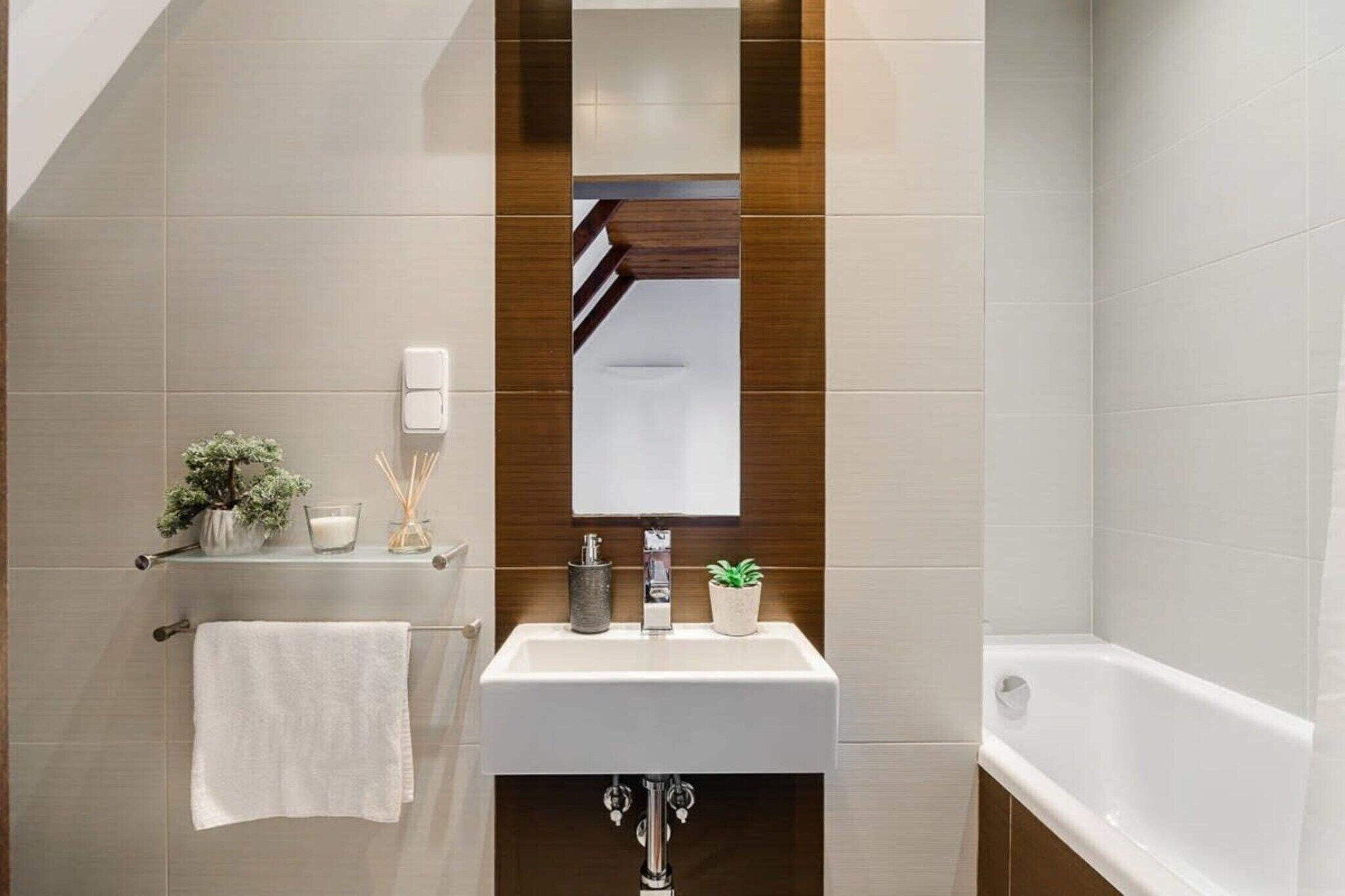 Une salle de bain moderne avec un lavabo blanc, un miroir et une baignoire. On y trouve un porte-serviettes avec une serviette blanche et une petite plante accrochée au mur.