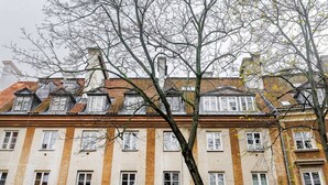 En bygning med flere etager, en række vinduer og et træ i forgrunden.