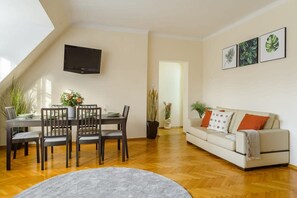 Ein modernes Wohnzimmer mit Essbereich, einem an der Wand montierten Flachbildfernseher und einer Couch mit dekorativen Kissen.