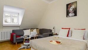 A cozy bedroom with a bed, a sofa, a small table with a laptop, and a window.
