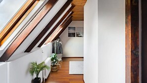 A narrow hallway with wooden beams, a radiator, a potted plant, and a coat rack with clothes.