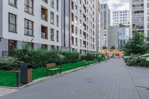 Een moderne straat in de stad met meerlaags woongebouwen, een groen ingericht gebied met banken en een helder voetpad.