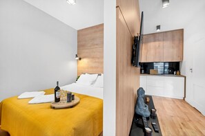 A modern hotel room with a bed, a small table with a bottle and glasses, a wall-mounted TV, and a kitchenette. - House in Landunvez near Plage de Penfoul (Warszawa)