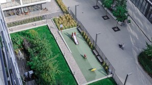 Ilmakuva modernista rakennuksesta, jossa on kattopuutarha, lasten leikkialue ja päällystetty kävelyreitti.