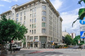 A multi-story building with a corner entrance, storefronts on the ground floor, and a pedestrian crossing. - House in Saint-Pabu near Stunning Beaches (Warszawa 2)